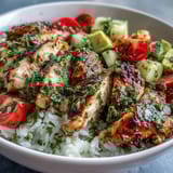 Perfectly grilled chimichurri chicken slices rest over fluffy rice with avocado, cherry tomatoes, and cucumber.