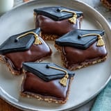 Close-up of buttery sugar cookies shaped like graduation caps, piped with glossy royal icing and colorful M&M details.  