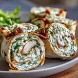 Close-up of turkey, cheese, and spinach tortilla pinwheels, highlighting creamy filling and fresh spinach leaves in soft tortillas.  