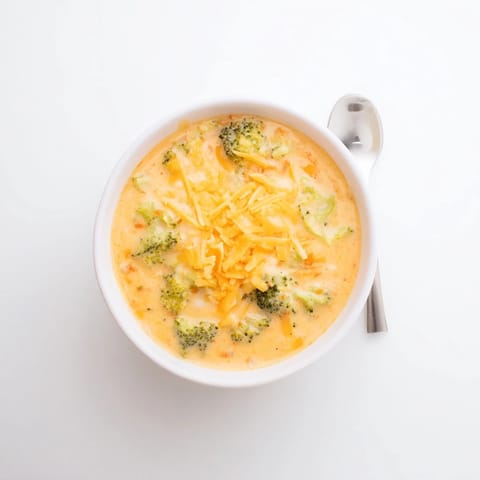 Steaming bowl of Broccoli Cheese Soup topped with shredded sharp cheddar and black pepper, served with crusty bread.