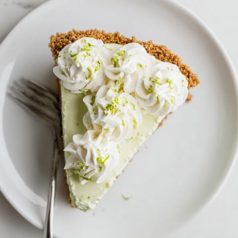 Chilled Key Lime Pie slice on a white plate showing creamy texture, graham cracker base, and a dollop of vanilla whipped cream.