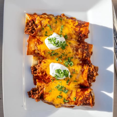 Rolled flour tortillas filled with seasoned ground beef and cheddar, smothered in red sauce and baked until bubbly and golden.