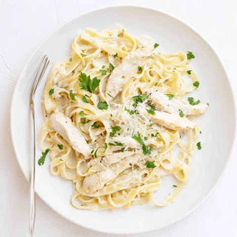 Tender sliced chicken breast served atop a steaming plate of cheesy Fettuccine Alfredo for a hearty meal.