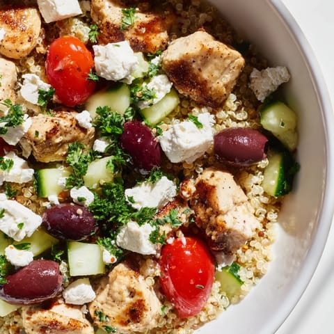 A close-up of the Mediterranean Chicken Bowl showing colorful vegetables and juicy chicken pieces on a light, textured surface.  