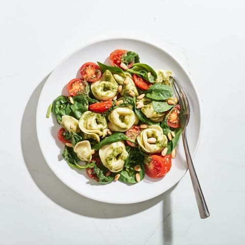Vibrant Pesto Tortellini Salad in a white bowl, highlighting melted Parmesan and herb flecks over tender cheese tortellini.  