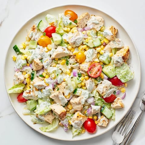 A close-up of Ranch Chicken Chopped Salad in a white bowl, featuring crisp romaine, juicy tomatoes, corn, and creamy dressing.