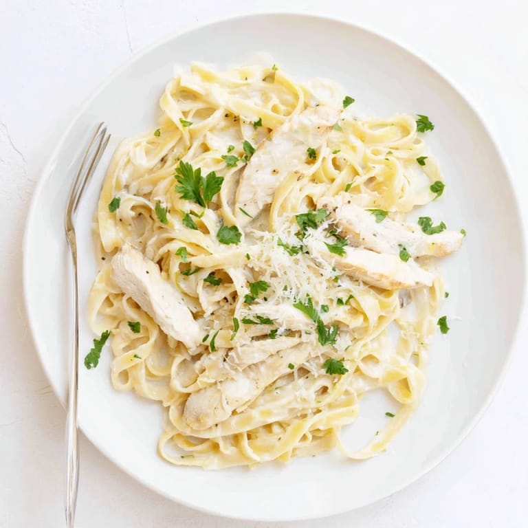 Tender sliced chicken breast served atop a steaming plate of cheesy Fettuccine Alfredo for a hearty meal.