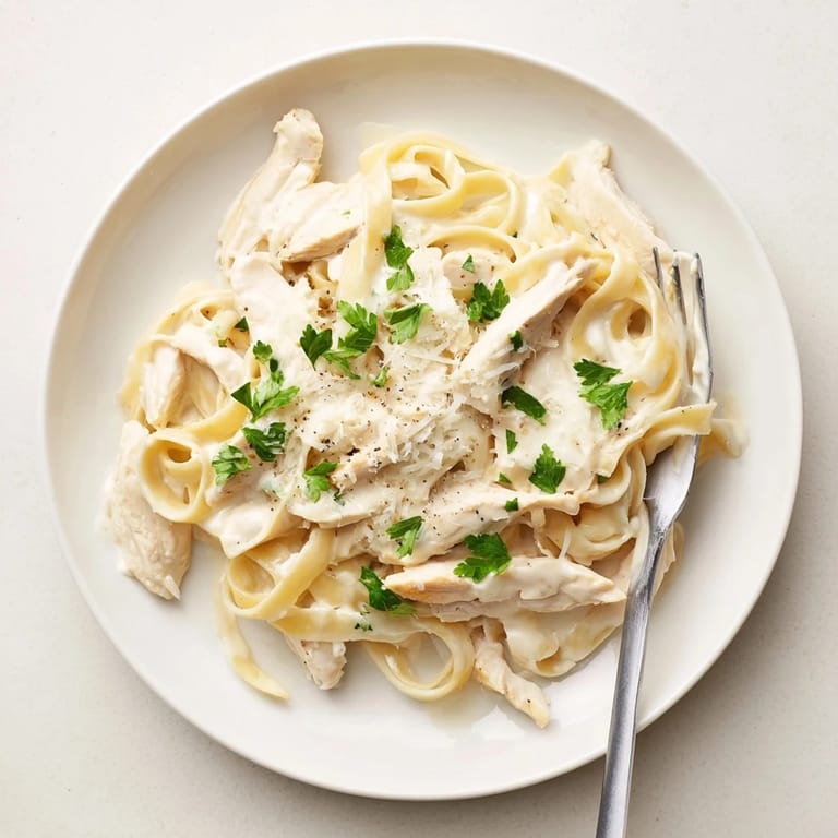 Homemade Fettuccine Alfredo plated with a golden-brown chicken breast, garnished with parsley and grated Parmesan cheese.