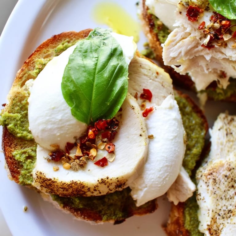 Golden Pesto Chicken Burrata Toast with fresh basil garnish, served warm on a rustic wooden board.  