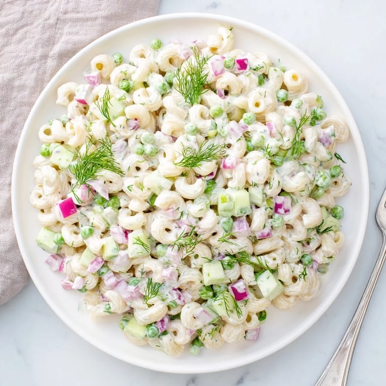 A close-up view of Creamy Dill Pickle Pasta Salad garnished with fresh dill and served on a platter.