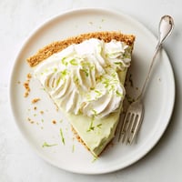 Freshly baked Key Lime Pie with a golden graham cracker crust and bright green filling, topped with fluffy whipped cream and lime zest.