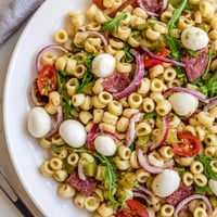 A vibrant Spring Antipasto Pasta Salad features ditalini, salami, mozzarella, and arugula tossed in a zesty vinaigrette.