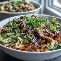 Golden-brown seasoned pork and crisp veggies rest on tender rice noodles in a steaming bowl of Potsticker Noodle Bowls.