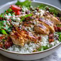 Golden-brown, marinated chicken slices from Sun-Dried Tomato Chicken Bowl rest on fluffy rice with fresh arugula and cherry tomatoes.
